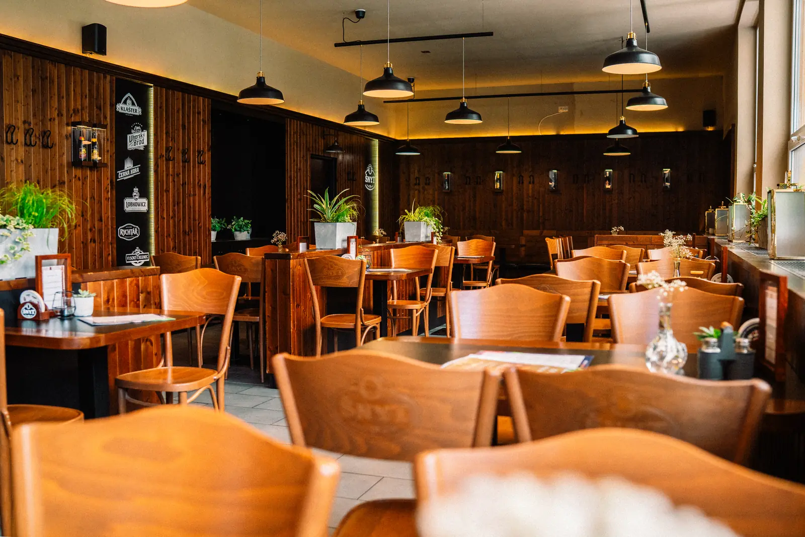 Prostorný sál restaurace ŠNYT s dřevěným obkladem, ohýbanými židlemi a závěsnými lampami