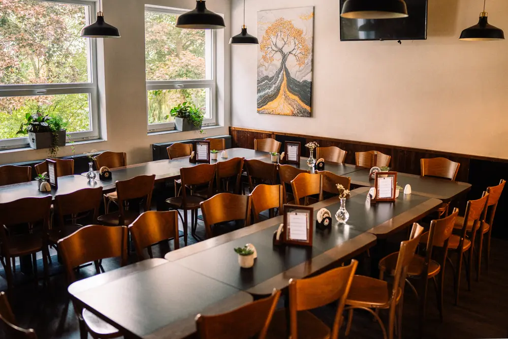 Salonek restaurace ŠNYT s dlouhými prostřenými tabulemi, malbou stromu na stěně a velkými okny